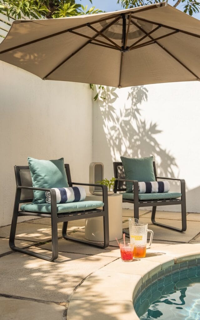 Poolside lounge, outdoor chairs, weatherproof cushions, striped towels, cantilever umbrella, no humans, sunlit concrete, pool water, outdoor speaker, frosty drinks, summer vibes, shade elements, relaxed atmosphere